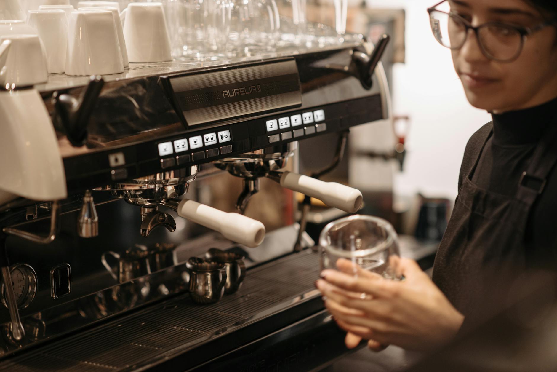 Barista w czarnym fartuchu przygotowuje espresso w przytulnej kawiarni