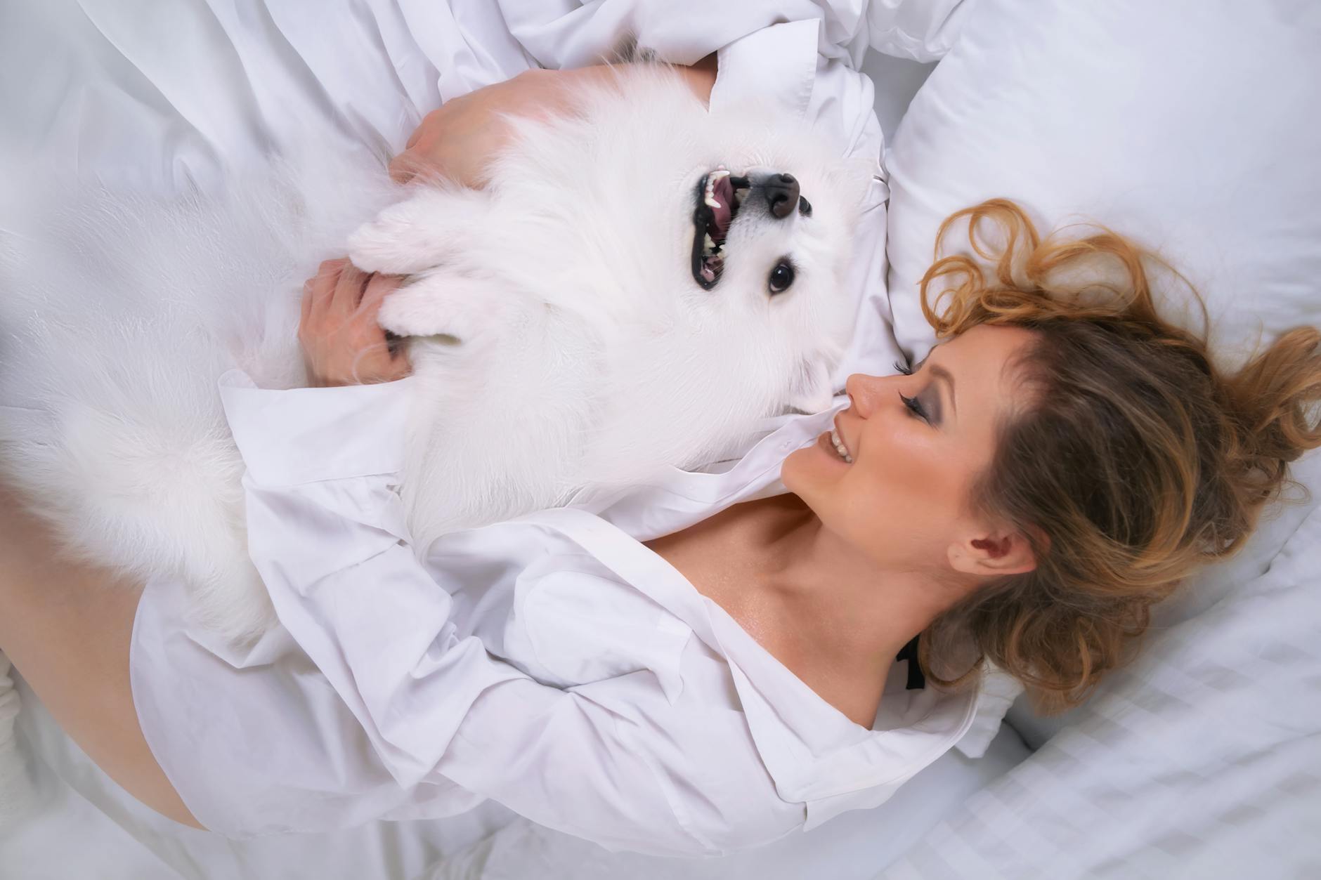 Kobieta przytula psa pomeraniana na białym łóżku, odpoczywa w sypialni
