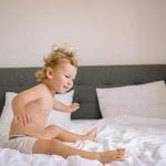 Uśmiechnięte dziecko skacze po łóżku w jasnej, przytulnej sypialni