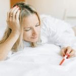 Kobieta leżąca na łóżku patrzy zamyślona na test ciążowy