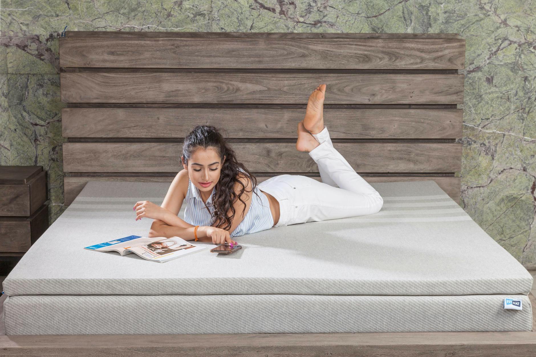 Młoda kobieta wypoczywa na łóżku z piankowym materacem, czytając magazyn