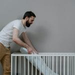 Mężczyzna montujący dziecięce łóżeczko w jasnym, minimalistycznym pokoju