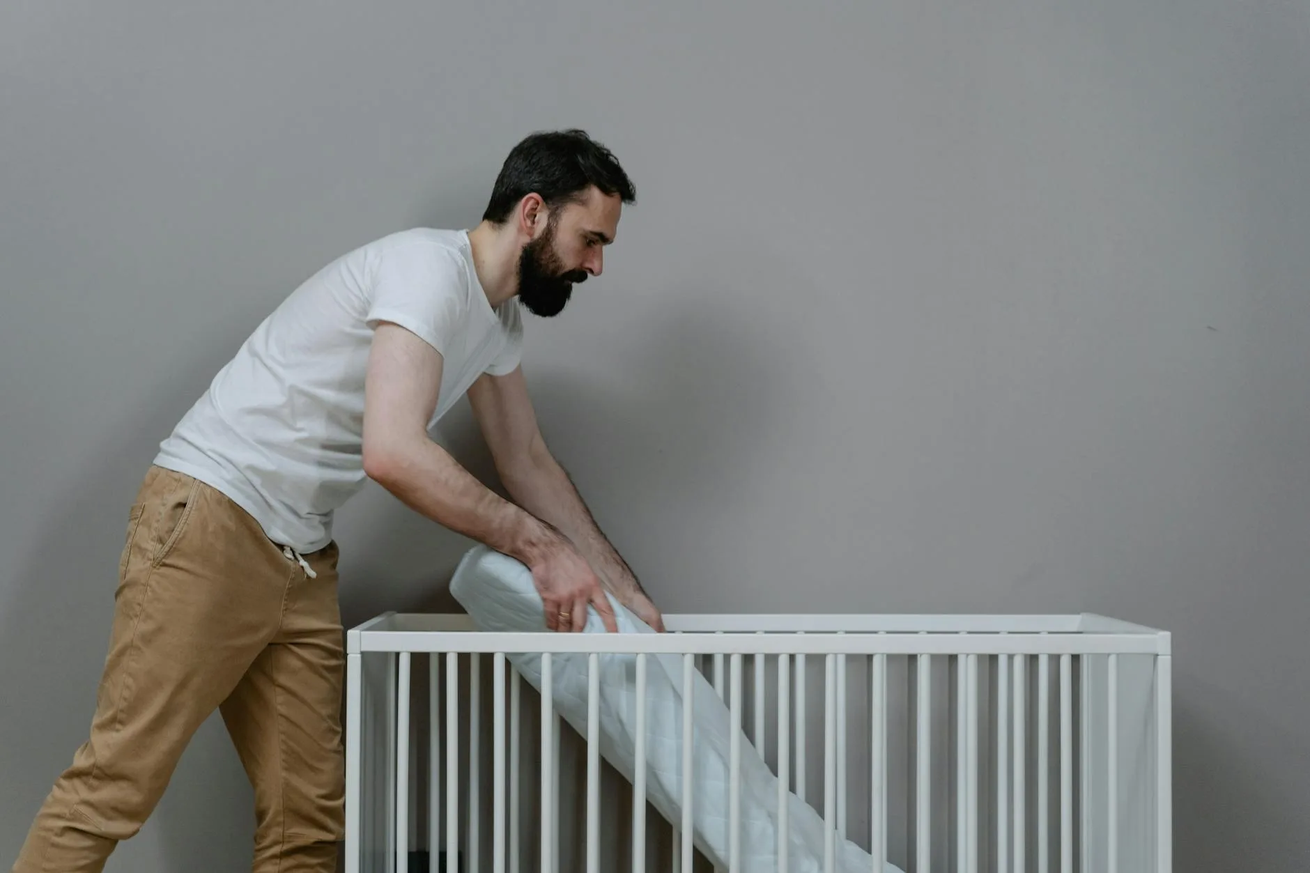 Mężczyzna montujący dziecięce łóżeczko w jasnym, minimalistycznym pokoju