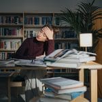 Zmęczona kobieta nad książkami w bibliotece, walcząca ze snem