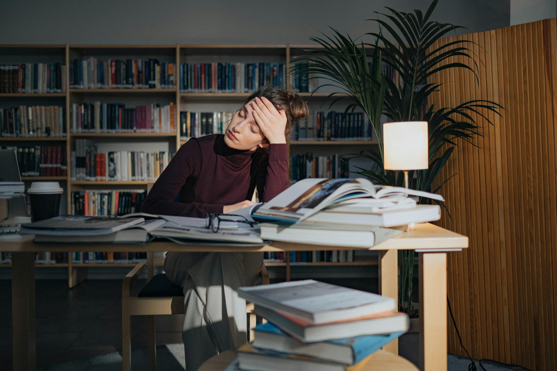 Zmęczona kobieta nad książkami w bibliotece, walcząca ze snem