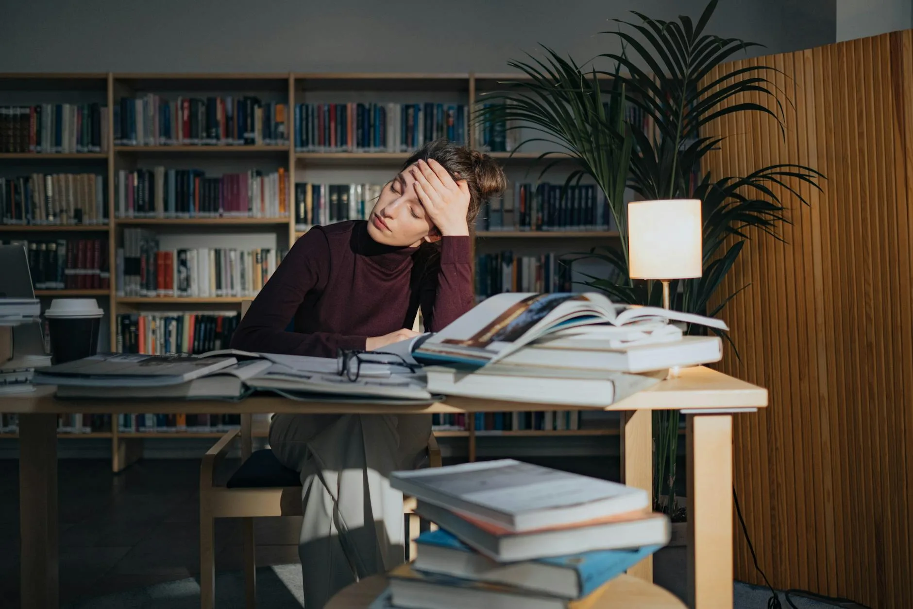 Zmęczona kobieta nad książkami w bibliotece, walcząca ze snem