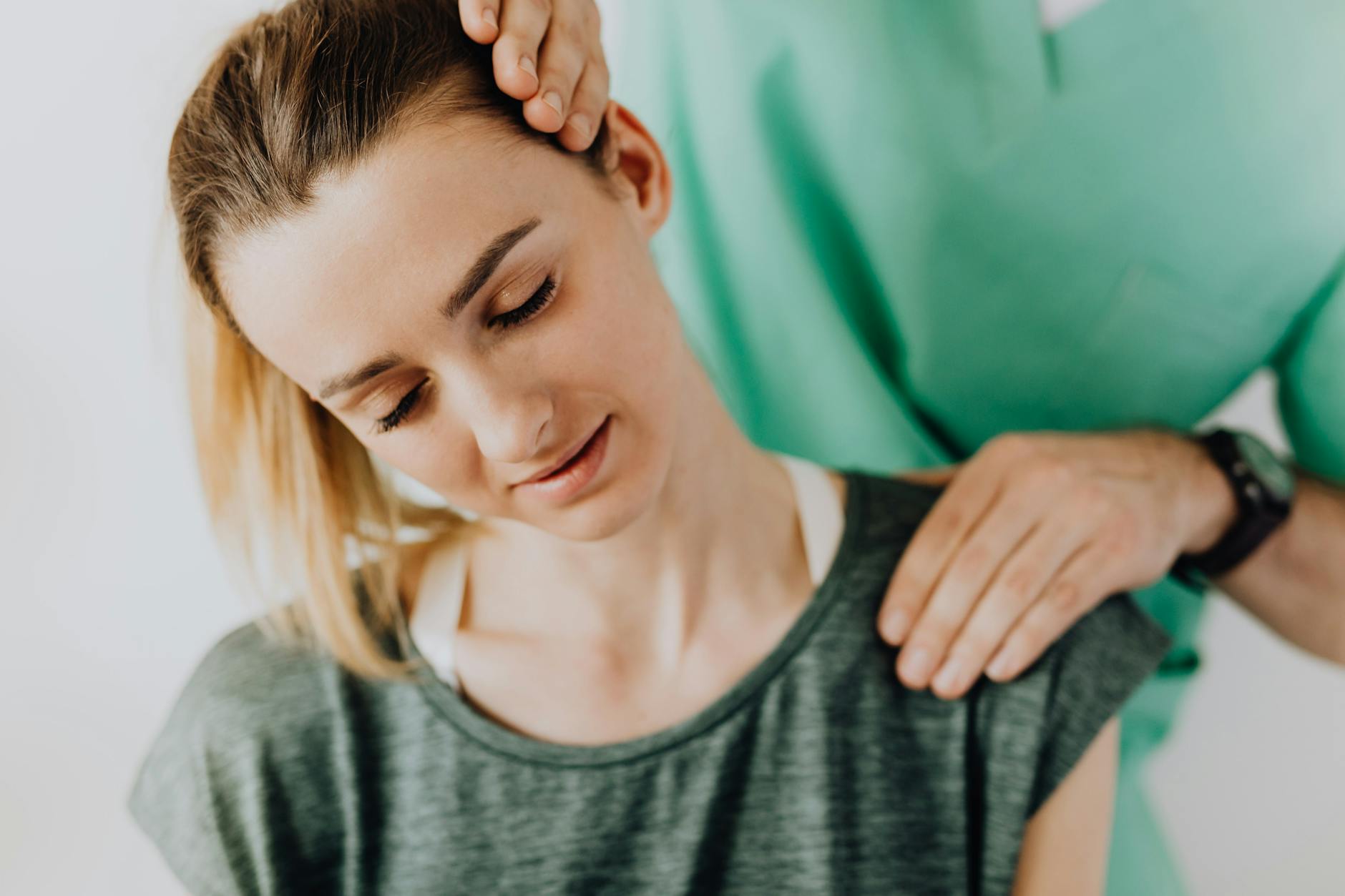 Fizjoterapeuta masuje kark uśmiechniętej kobiety z bólem szyi