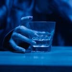 Dłoń trzymająca szklankę whisky nocą, symbol wieczornego picia alkoholu