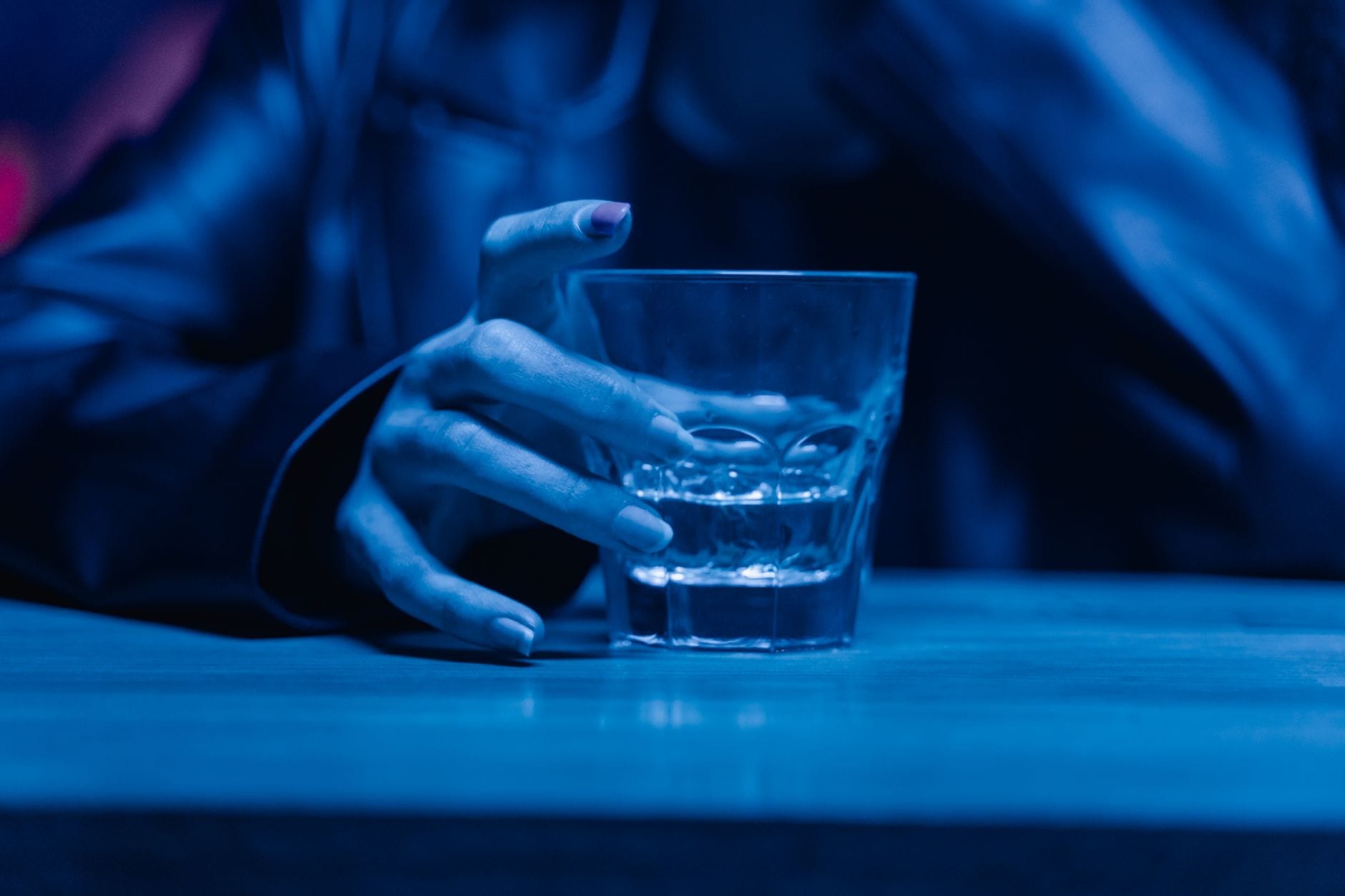 Co robi alkohol ze snem? Dlaczego zasypiasz szybciej, ale budzisz się gorzej Dłoń trzymająca szklankę whisky nocą, symbol wieczornego picia alkoholu