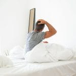 Mężczyzna rozciąga się rano w łóżku na materacu w jasnej sypialni