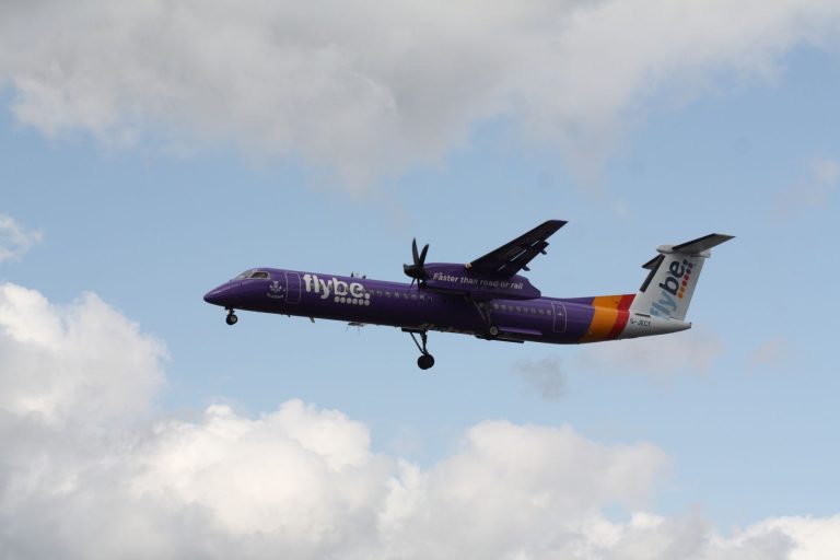 Samolot Flybe lecący przez częściowo zachmurzone niebo